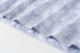 A close-up of a light lavender and white fabric with a floral damask pattern, showing the texture and folded edges.
