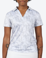 A woman wearing a short-sleeve collared polo shirt with a light gray and white tropical leaf pattern, shown from the chin down against a plain light background.