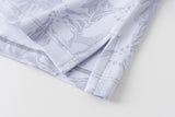 A close-up of a light-colored fabric with a subtle lavender floral pattern, showing folded edges and neat stitching on a plain white background.