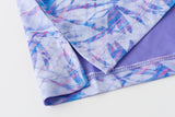 Close-up of a folded garment showing a light purple and blue abstract leaf pattern on the exterior and a solid lavender interior lining, with a decorative zigzag stitched hem.